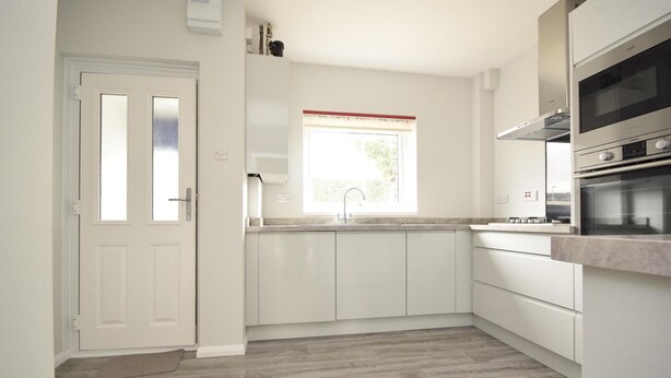A modern kitchen with white cabinets, a built-in oven, and a window with a red frame. - Comfy modern townhouse/w free parking & garden, newly refurbished, self catering (Cheltenham)