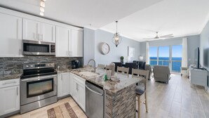 A modern kitchen with a large island, stainless steel appliances, and a view to the ocean.