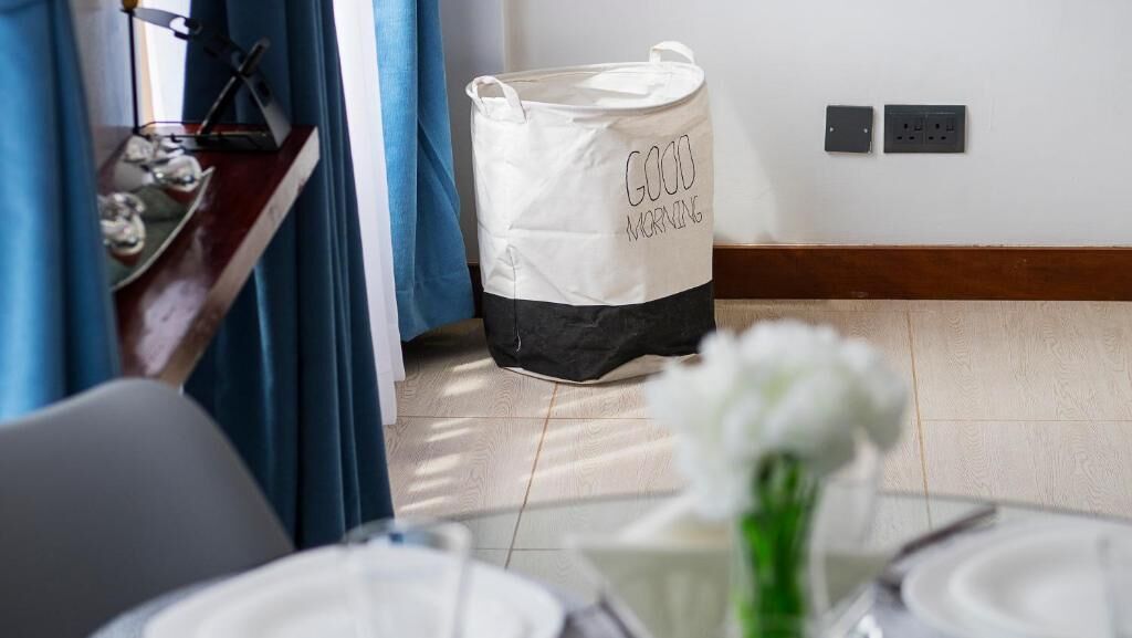 A dining area with a table set for two, a white flower vase, and a storage bag with "GOOD MORNING" text.