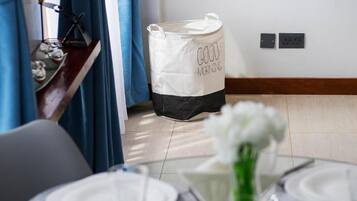 A dining area with a table set for two, a white flower vase, and a storage bag with "GOOD MORNING" text.