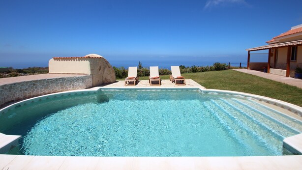 A swimming pool with three lounge chairs, a stone wall, and a view of the ocean. - A detached vacation home with country house charm (CN)