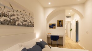 A bedroom with a bed, a desk, and a chair. There is a painting on the wall and a plant in the corner. - nota-Mi - Domus Ticinese (Milan)