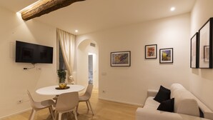 A modern living room with a dining area, a flat-screen TV mounted on the wall, and a sofa with cushions. - nota-Mi - Domus Ticinese (Milan)