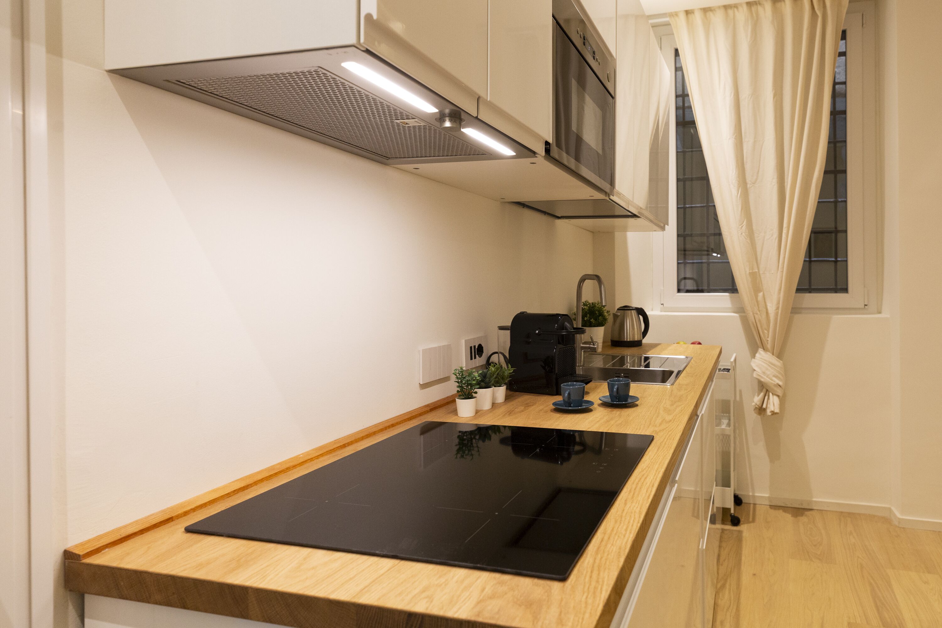 A modern kitchen with a black induction cooktop, stainless steel appliances, and a wooden countertop.