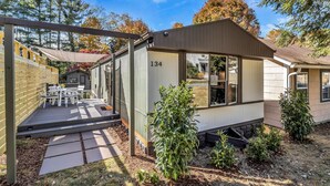 A mobile home with a patio area, number 134, surrounded by small shrubs and a wooden fence.
