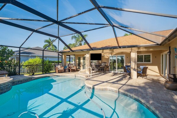A swimming pool with a covered patio area, outdoor furniture, and a view of neighboring houses.