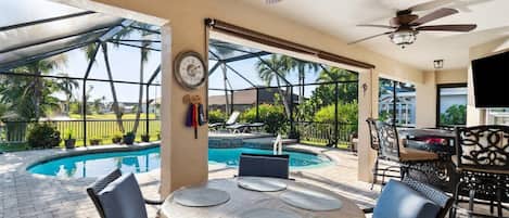 An outdoor patio with a pool, dining table, chairs, and ceiling fans.