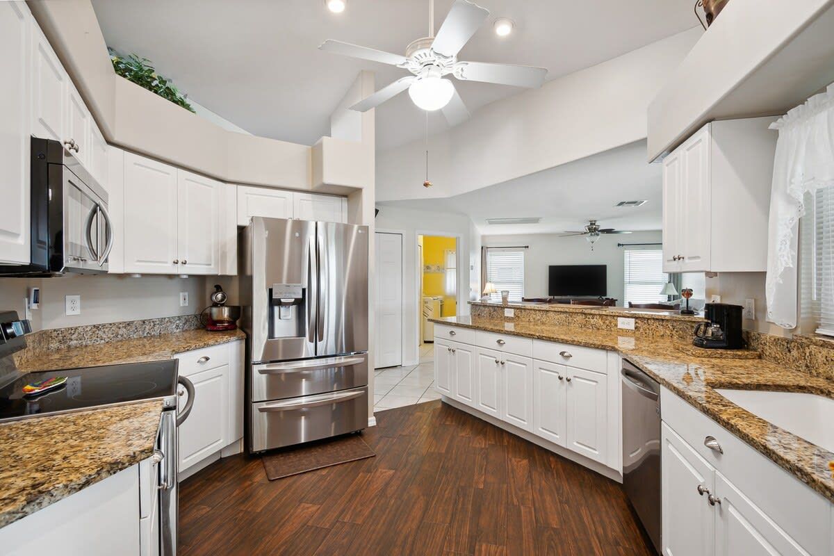 A modern kitchen with white cabinets, stainless steel appliances, granite countertops, and a ceiling fan.