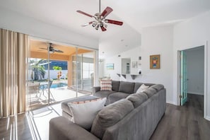 Een moderne woonkamer met een grijze modulaire bank, een plafondventilator en een glazen deur naar een zwembad.