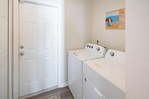 A laundry room with a white door, two white washing machines, and a painting on the wall.