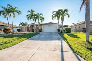 Un vialetto residenziale conduce a una casa con garage, circondata da palme e prati curati.