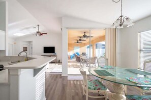 Una cocina moderna con una mesa de comedor de vidrio, armarios blancos y un ventilador de techo.