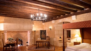 A room with a wooden ceiling, stone walls, a bed with a red headboard, a table with chairs, and a chandelier. - Hapimag Château de Chabenet (Le Pont-Chretien-Chabenet)