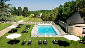 A rectangular pool with a stone border, surrounded by lounge chairs and umbrellas, set against a backdrop of trees and a distant building. - Hapimag Château de Chabenet (Le Pont-Chretien-Chabenet)