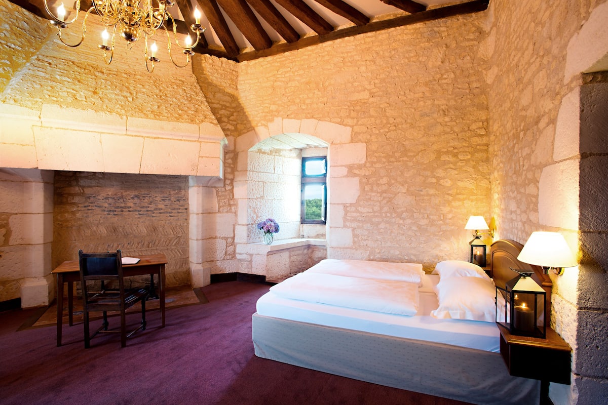 A bedroom with a stone wall, a bed, a desk, and a chair.