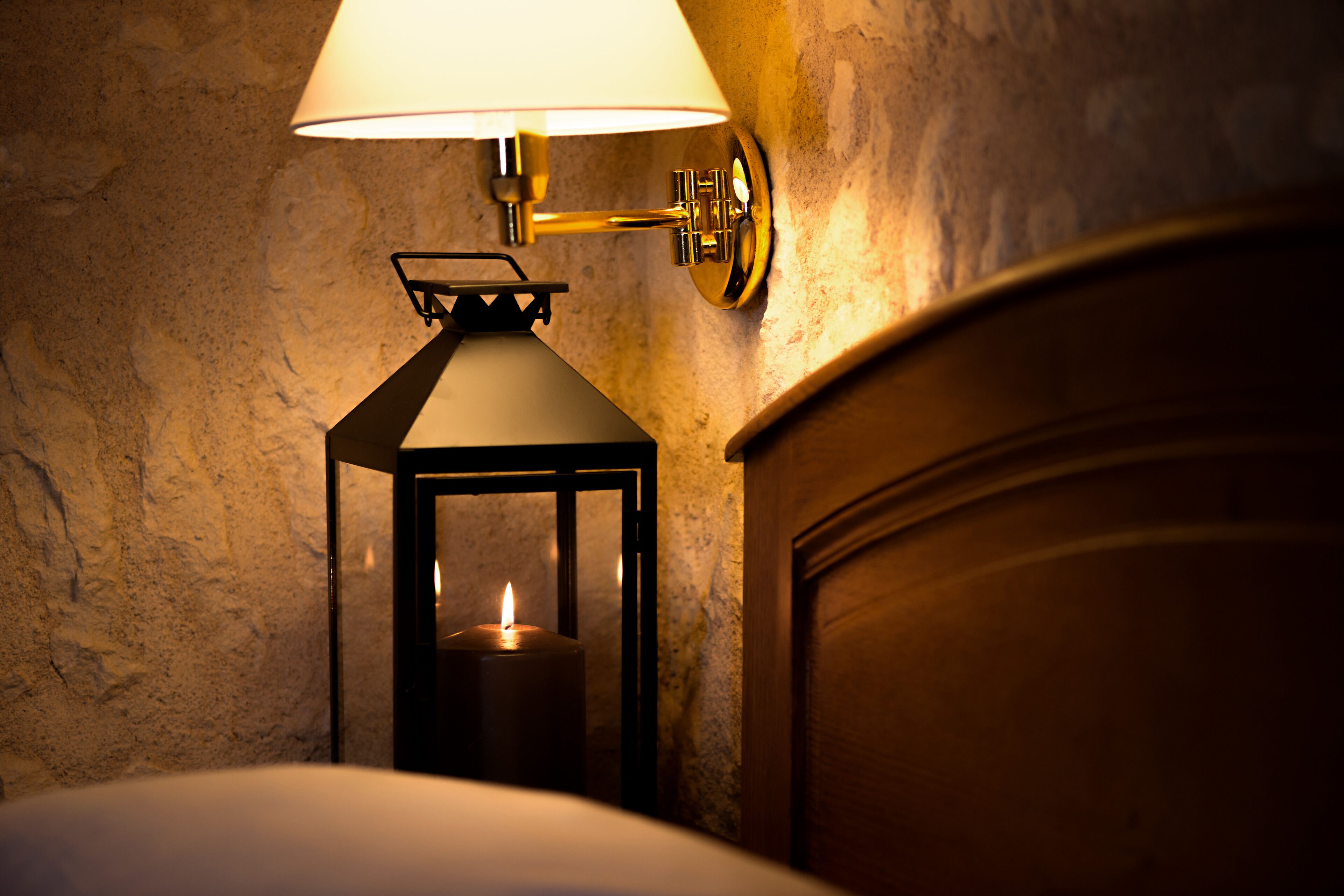 Una lámpara de pared con una vela en su interior, una puerta de madera y un muro con textura.