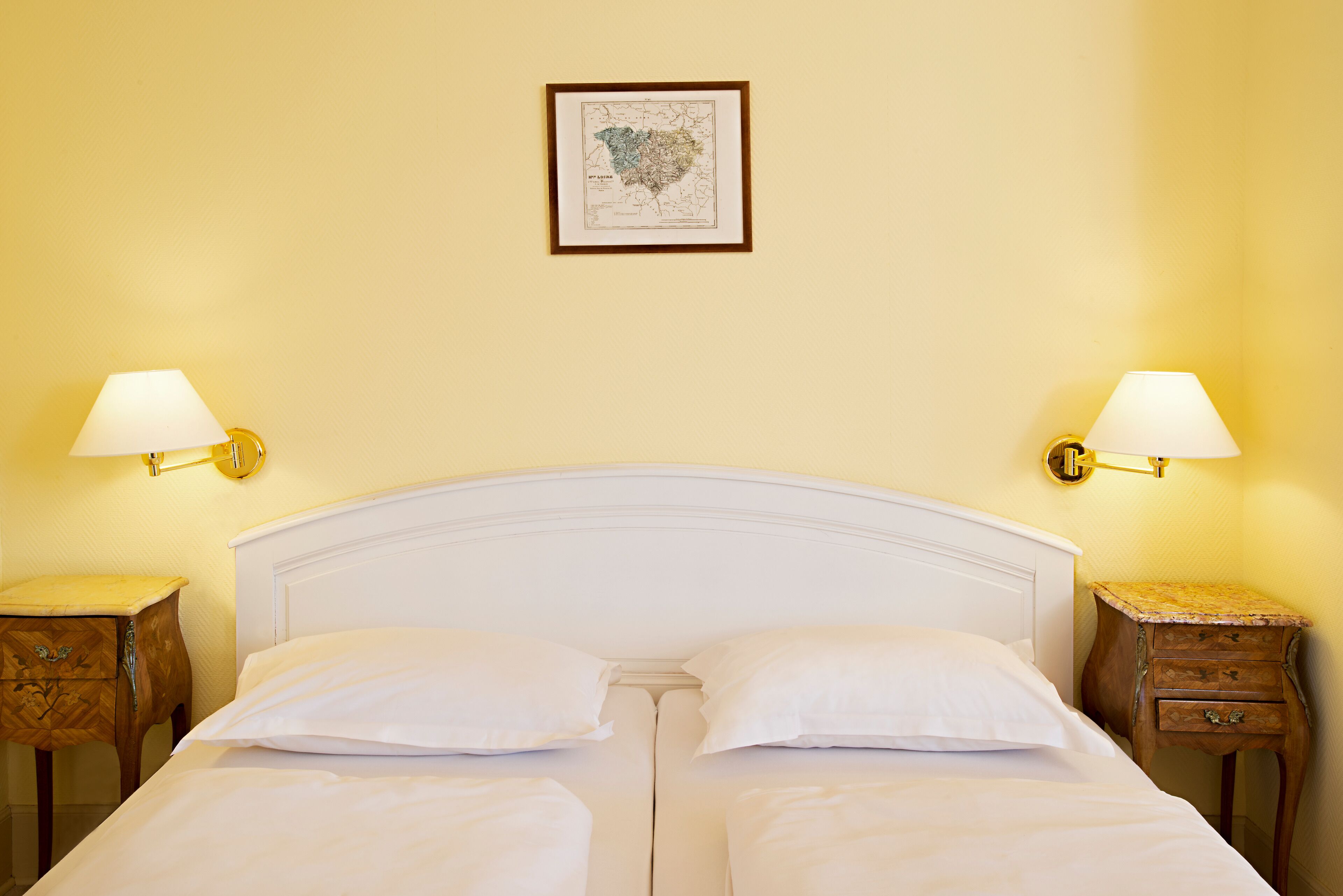 Una cama doble impecablemente arreglada con sábanas blancas, dos mesitas de noche con lámparas, y un mapa enmarcado en la pared.