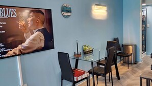 A modern living room with a flat-screen TV, a dining area with a glass table and chairs, a wall clock, and a built-in shelf. - Oceanfront Efficiency T604 (Myrtle Beach)