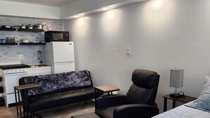 A compact room with a kitchenette, a sofa, a chair, a bedside table, and a bed. - Oceanfront Efficiency T604 (Myrtle Beach)