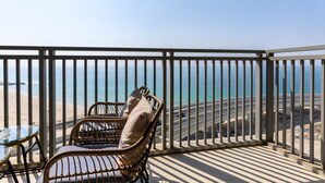 Ein Balkon mit Korbmöbeln und einem Glastisch, mit Blick auf Strand und Meer.