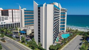 Un hôtel de grande hauteur, avec de nombreux étages, une piscine et une vue sur la plage.