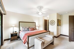 Un dormitorio con cama, mesitas de noche, un banco, un ventilador de techo y una puerta.