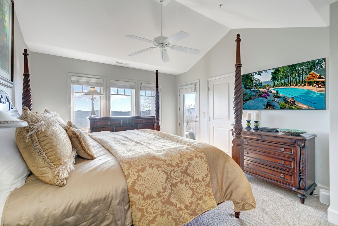 A bedroom with a four-poster bed, a ceiling fan, and a large TV displaying a tropical scene.
