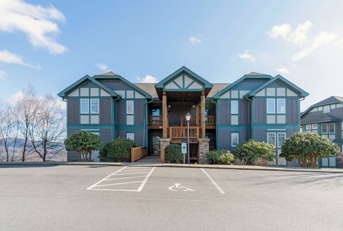 A multi-story building with a central entrance, a handicap parking space, and a view of the surrounding area.