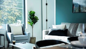 A modern living room with a grey sofa, a small armchair, a coffee table, and a potted plant. - Ski & Tee Retreat - Bright Three Bedroom + Hot Tub (Revelstoke)