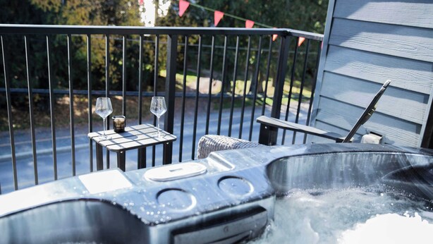 A hot tub with two glasses and a container on a table, surrounded by a metal fence and a house in the background. - Ski & Tee Retreat - Bright Three Bedroom + Hot Tub (Revelstoke)