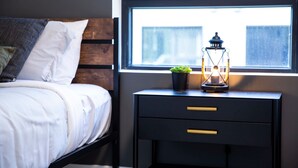 A bed with white bedding, a nightstand with a lamp, and a window with a view of buildings. - Ski & Tee Retreat - Bright Three Bedroom + Hot Tub (Revelstoke)