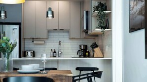 A modern kitchen with a wooden dining table, black chairs, a white countertop, and a hanging plant. - Ski & Tee Retreat - Bright Three Bedroom + Hot Tub (Revelstoke)