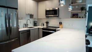 A modern kitchen with stainless steel appliances, a white marble countertop, and a built-in microwave. - Ski & Tee Retreat - Bright Three Bedroom + Hot Tub (Revelstoke)