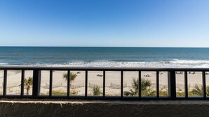 A beach view from a balcony with a railing, sandy beach, and ocean.
