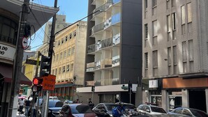 A multi-story building with balconies, a street with cars and pedestrians, and a visible sign for 'Av. C. Libero'. - Luz 1802 (São Paulo)