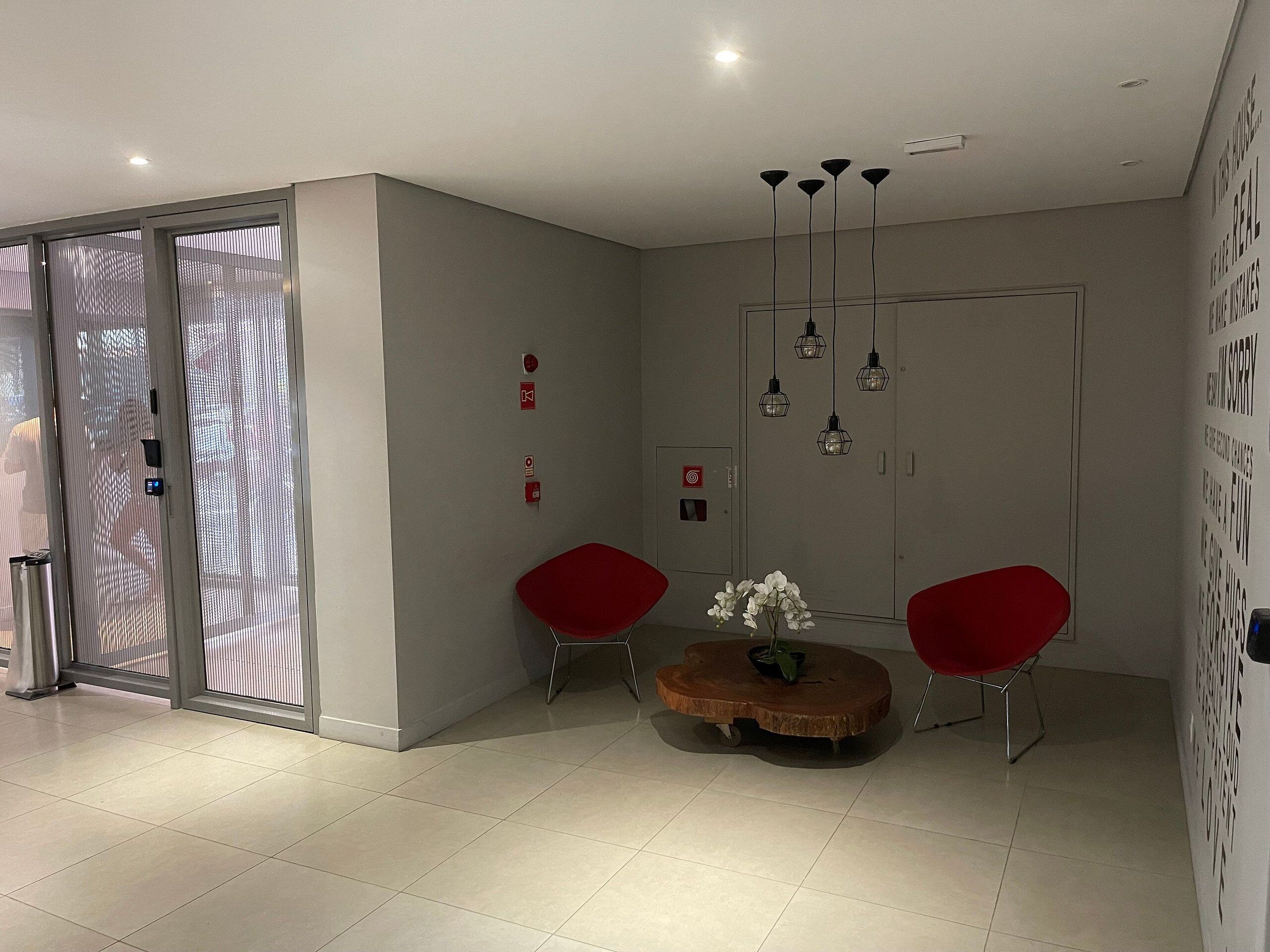Un área de espera moderna con puerta de vidrio, una mesa redonda de madera y sillas, y una pared con citas inspiradoras.