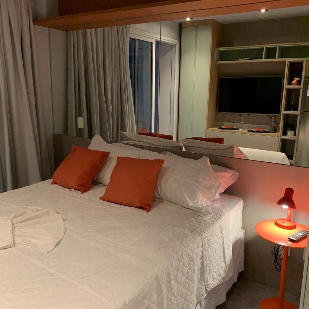 Une chambre d’hôtel avec un lit, une table de chevet avec une lampe, une télévision et une fenêtre avec des rideaux.