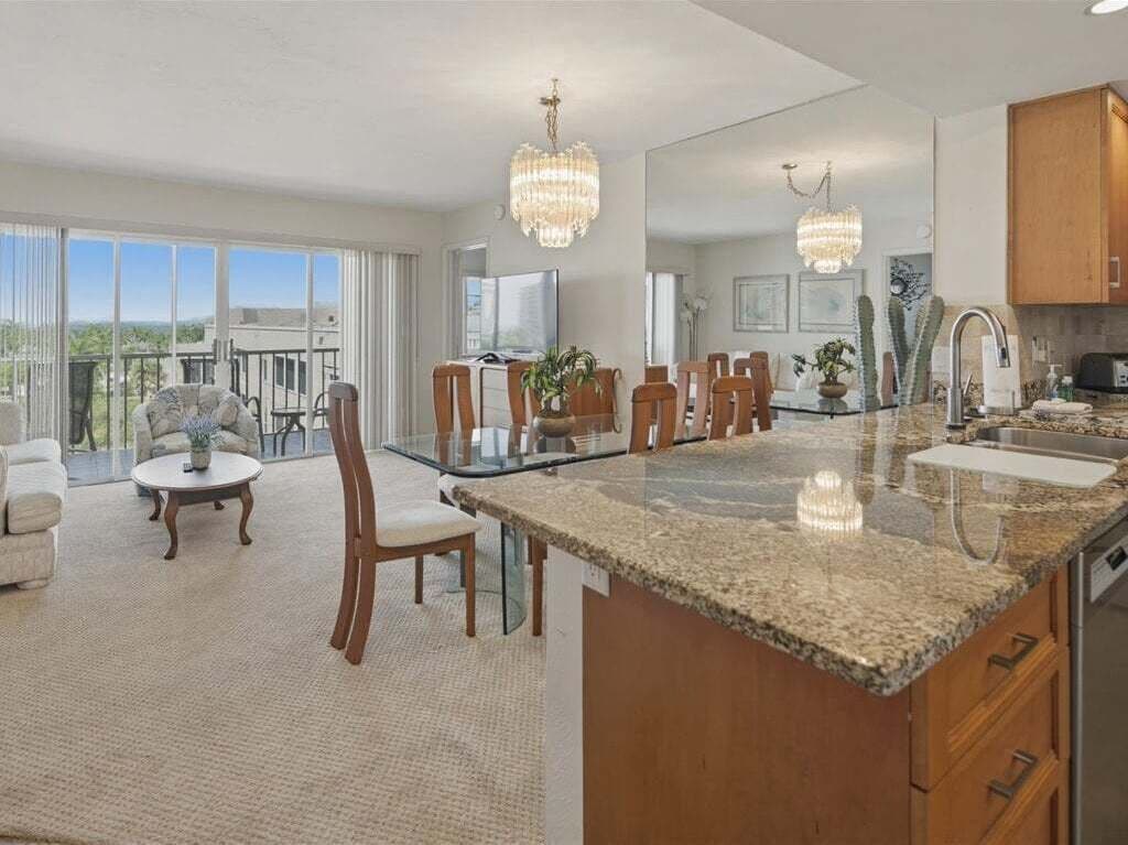 A spacious living area with a dining table, chairs, a coffee table, and a large window offering a view.