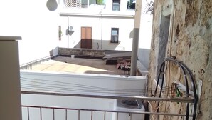 A balcony with a metal railing, a red bucket, and a white wall with exposed pipes.