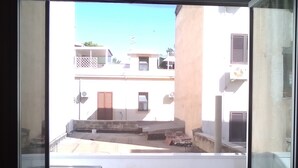 A view through a window of a building with multiple balconies, a wooden door, and air conditioning units.