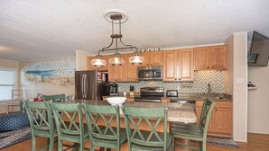 A kitchen with wooden cabinets, a central island, and a dining area with green chairs.