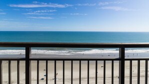 Une vue sur la plage depuis un balcon doté d’une balustrade, avec une plage de sable et l’océan en toile de fond.