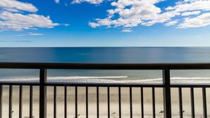 A beach view from a balcony with a railing, clear sky, and ocean. - Stay in Style with Our Oceanfront Room 11th Floor (Myrtle Beach)