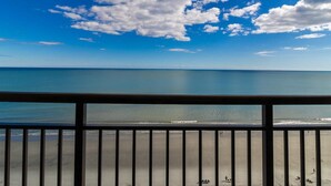 A beach view from a balcony with a railing, clear sky, and calm sea. - Soothing Waves Oceanfront Room 12th Floor (Myrtle Beach)