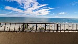 Une vue sur la plage depuis un balcon doté d’une balustrade, avec des palmiers et des parasols de plage.