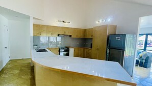 A modern kitchen with a curved island, wooden cabinets, stainless steel appliances, and a view to the outside. - Red Hibiscus Luxury Home (Avarua)