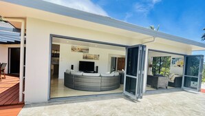 A modern house with a glass door leading to a living area featuring a large round seating area and a flat-screen TV. - Red Hibiscus Luxury Home (Avarua)
