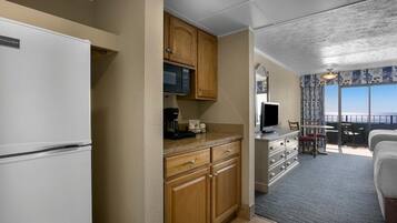A compact kitchen with wooden cabinets, a microwave, and a coffee maker. A dining area with a table and chairs is visible, leading to a balcony with a view.