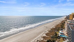 A beachside hotel with a long view of the ocean, a sandy beach, and a clear sky. - Penthouse Living Oceanfront Deluxe King Efficiency (Myrtle Beach)