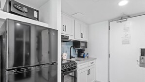 Una cocina compacta con un refrigerador de acero inoxidable, un microondas, una estufa y armarios blancos.